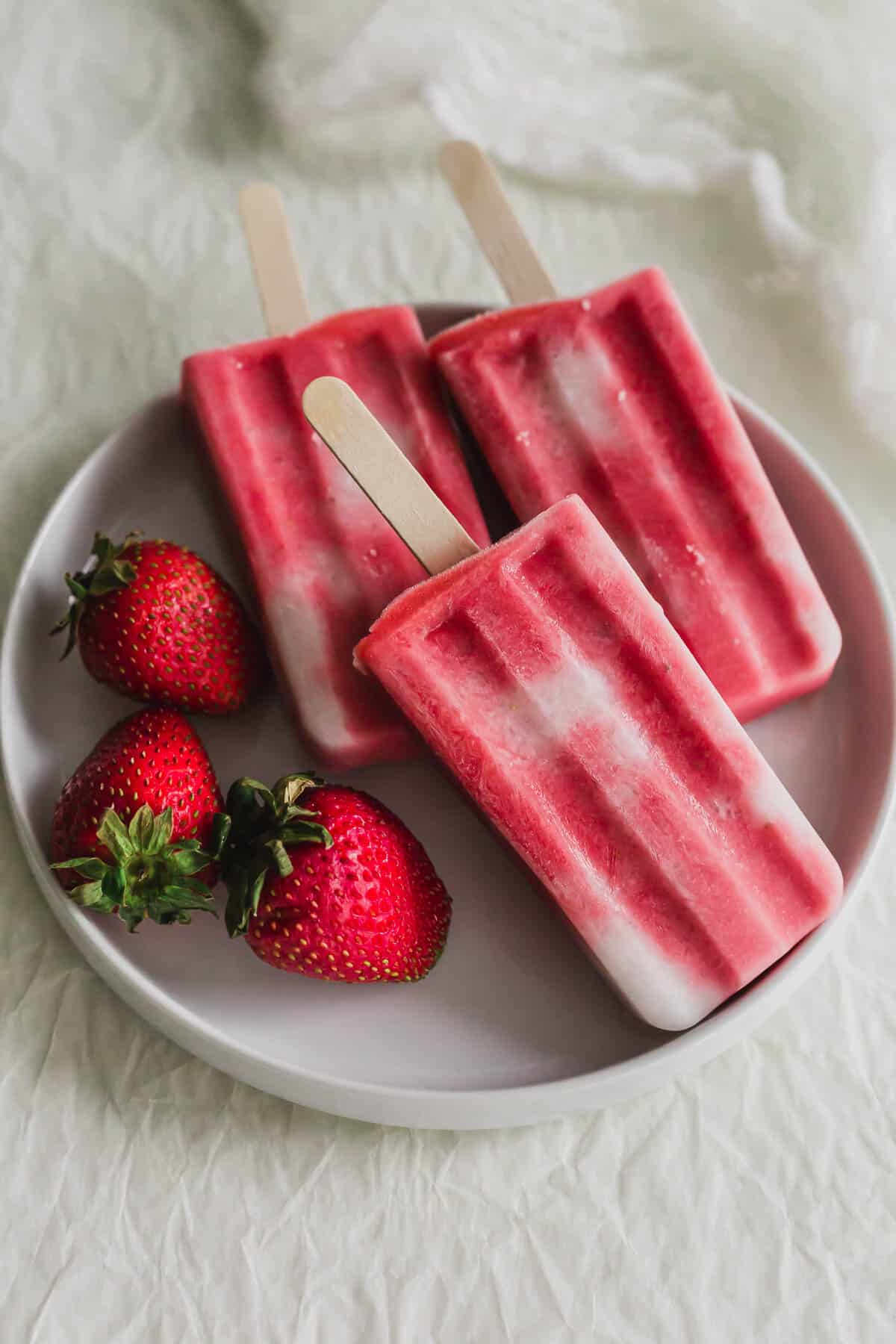 3 Strawberry sago popsicles on a white plate, with strawberries on the side.